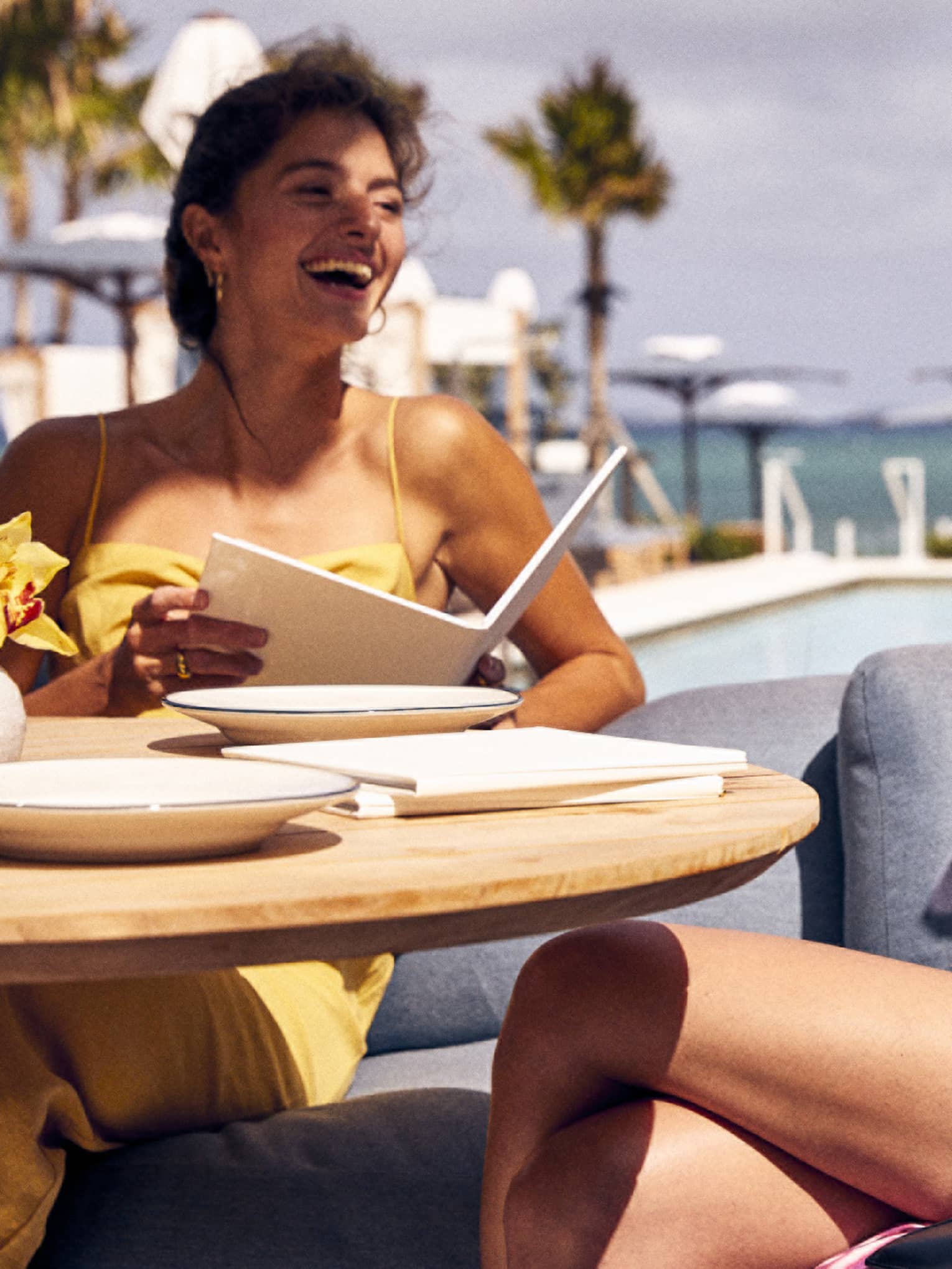 Two women talking in a sitting area outside with palm trees in the distance.