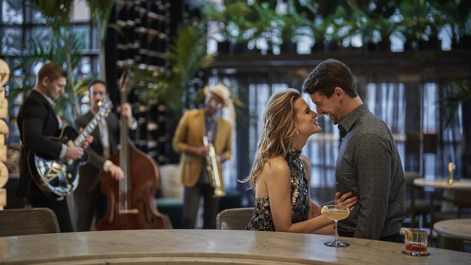 A man and woman sitting at a bar while a jazz band plays in the background.