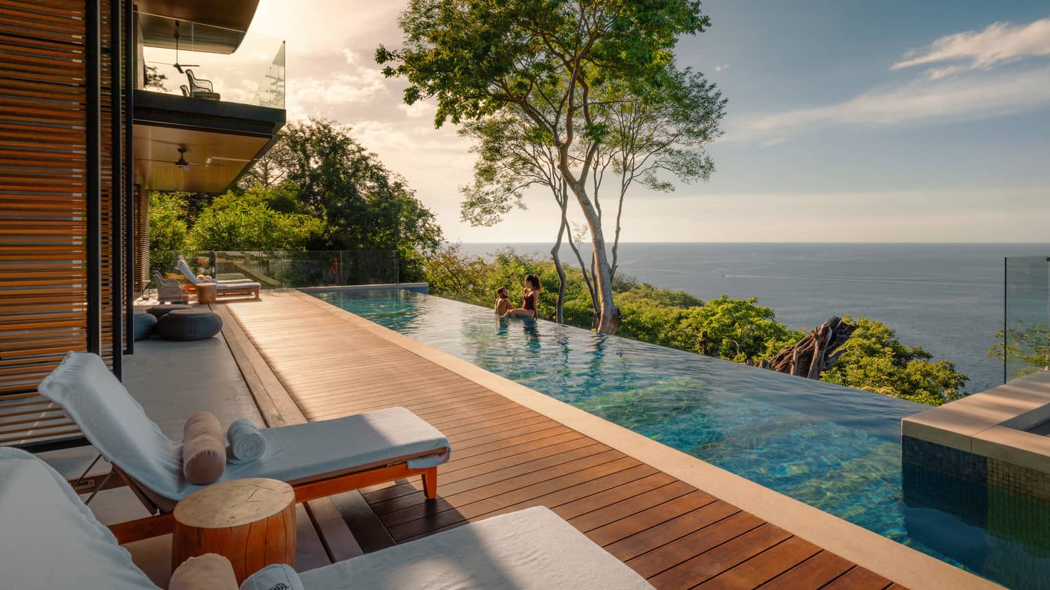 Large rectangular wooden deck and infinity pool overlooking a bay