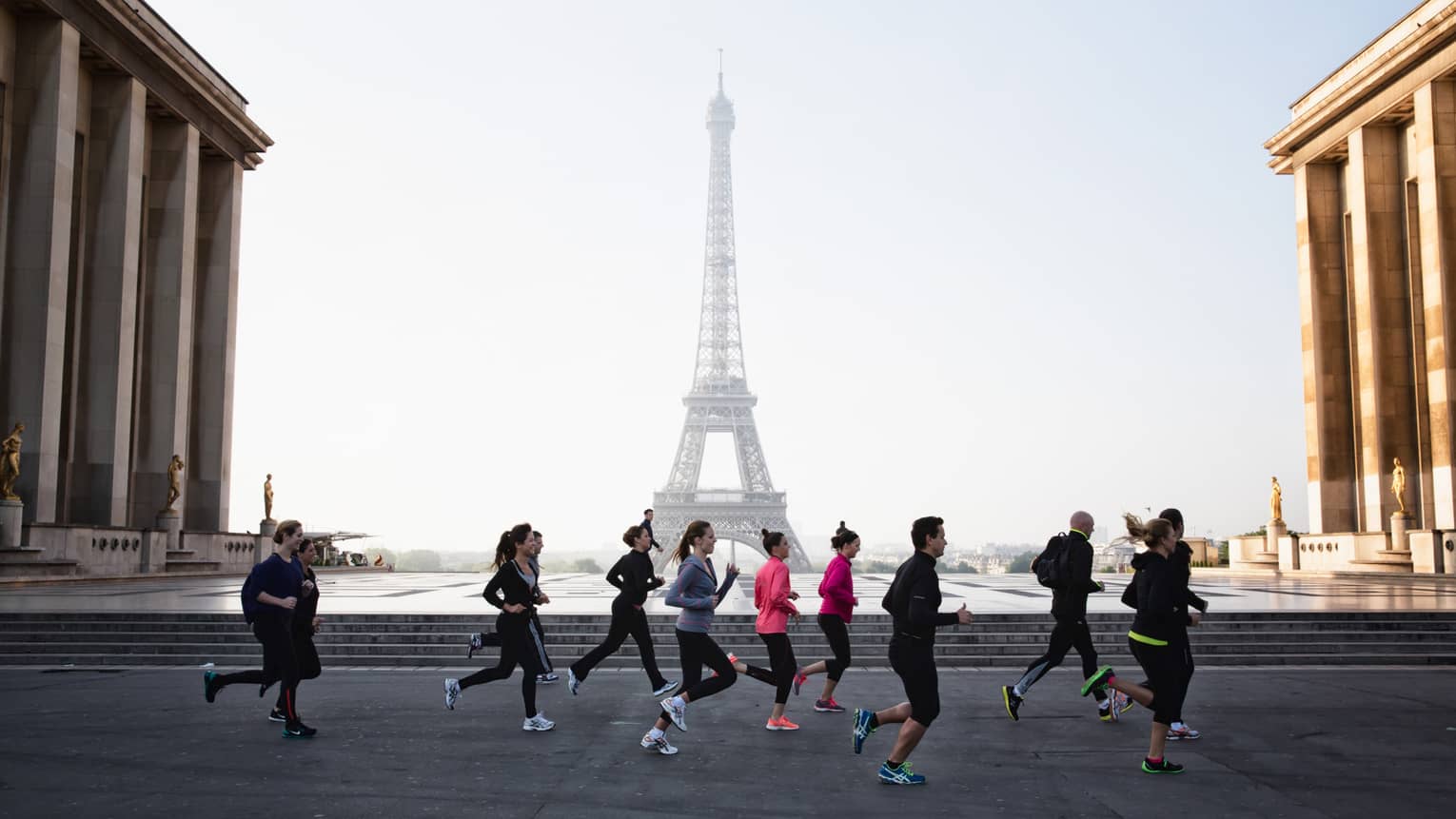 Group of runners jogs past Eiffel Tower on brick path