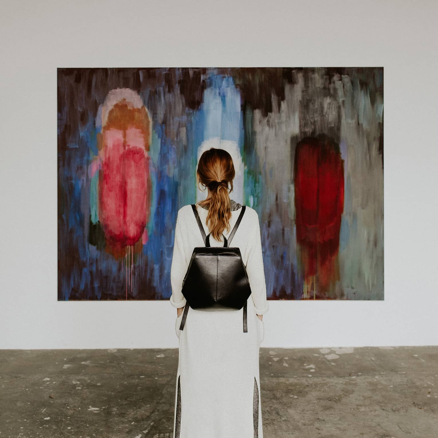 A person with a backpack standing in front of an abstract painting in an art gallery.