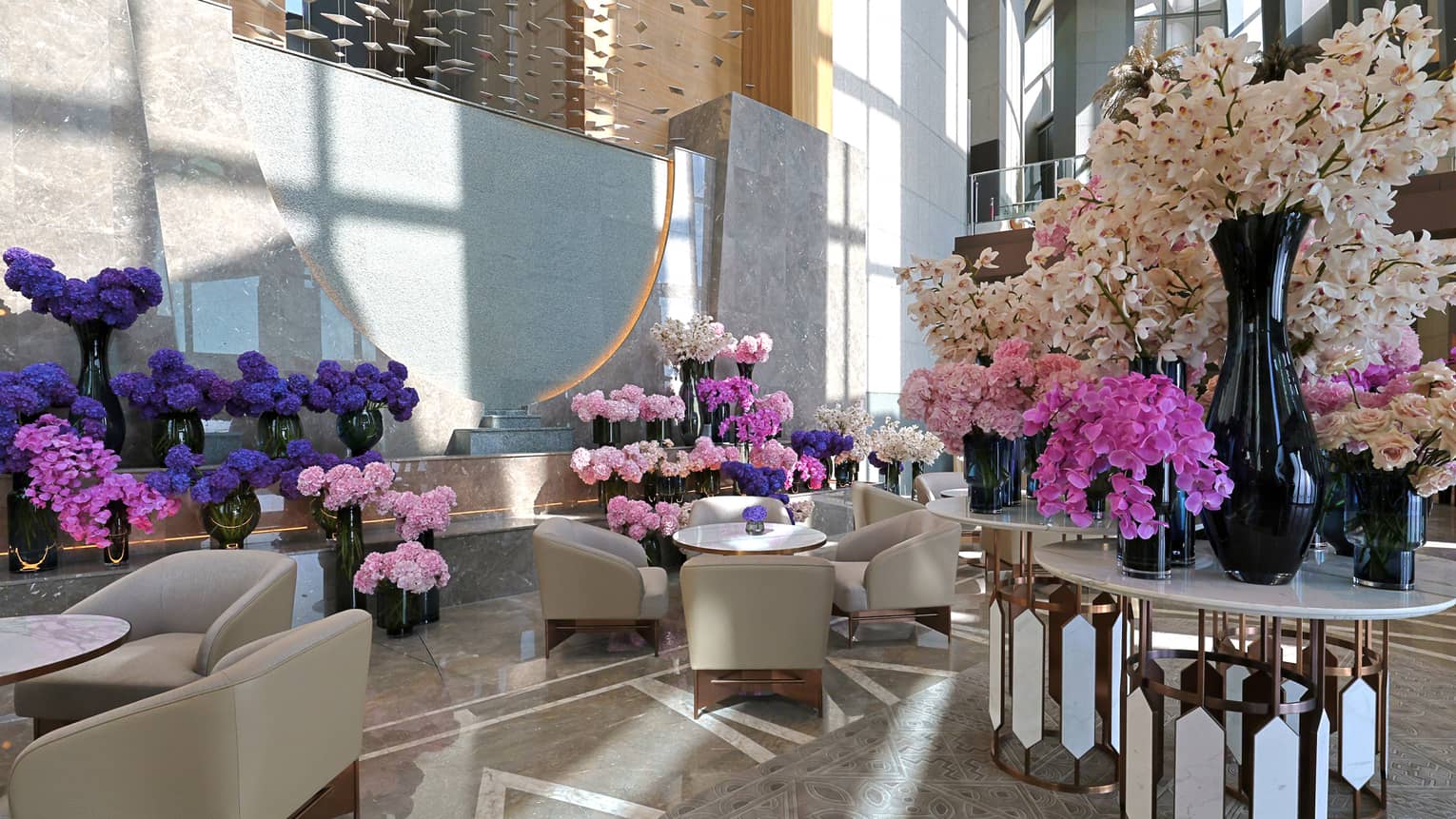 Hotel lobby with light-grey arm chairs and tables filled with pink, purple and white flowers