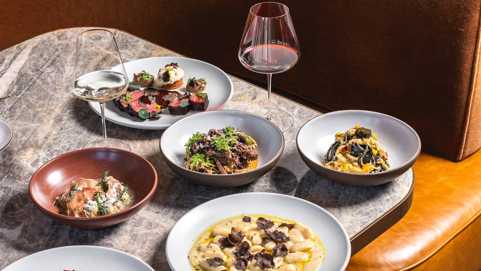 Plates of food and a wine glass set on a table at a booth in a restaurant