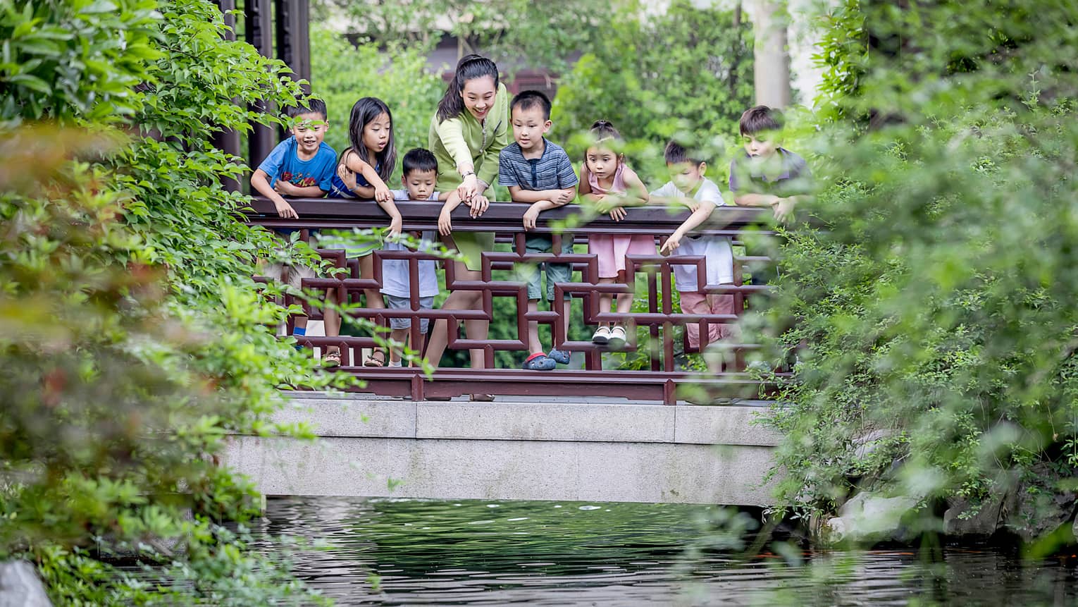 Children hang onto wood railing over water as hotel staff points below