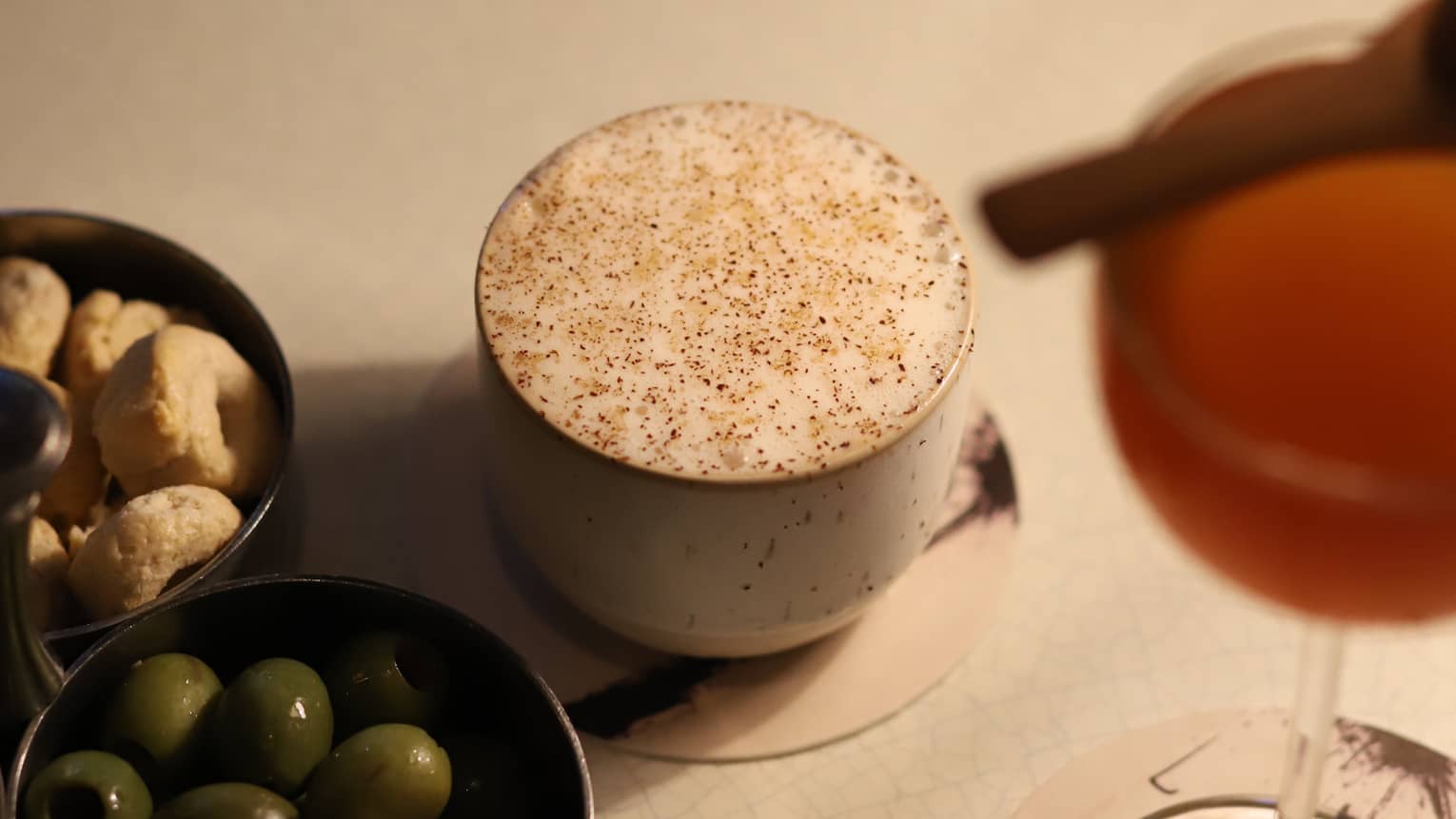 Two bowls of olives and peanuts set beside a coffee and wine glass