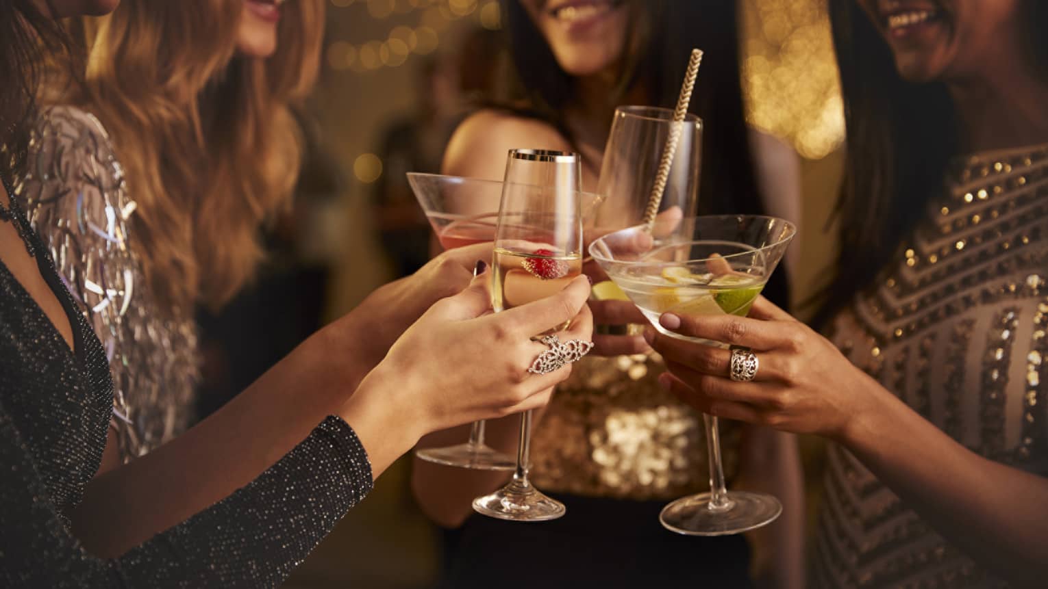 Four women in evening wear clink their cocktail glasses
