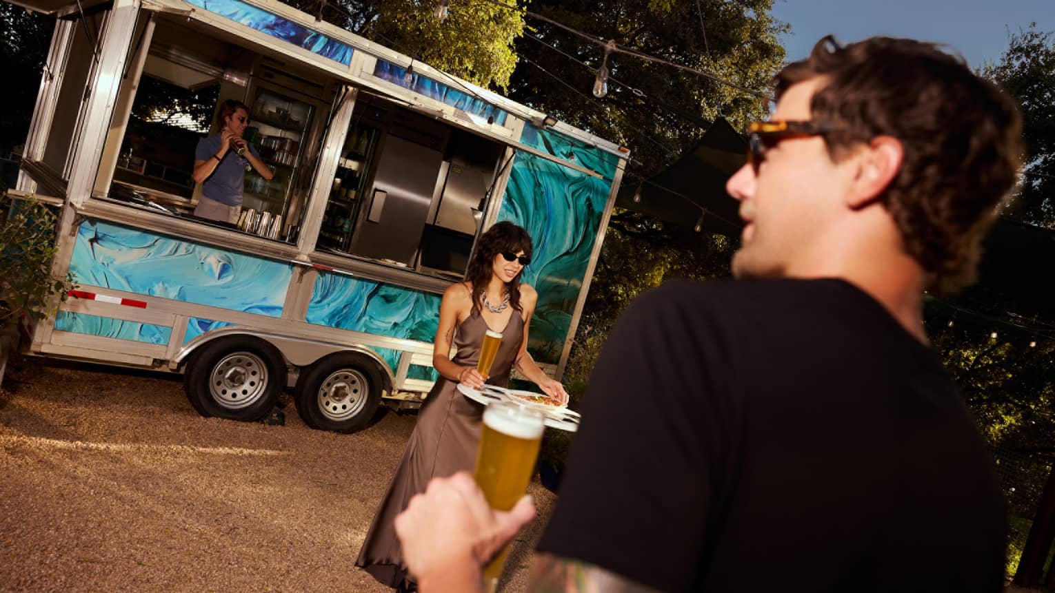 A couple dressed in formal attire holding tall glasses of beer in front of a blue food truck