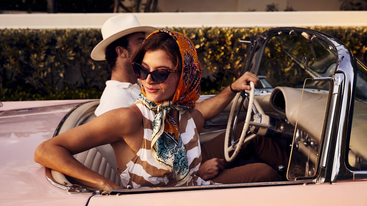 A woman in a scarf and a man in a hat in an old vintage car.