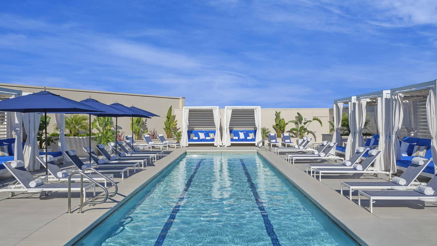 Pool with cabanas, lounge chairs and blue umbrellas.