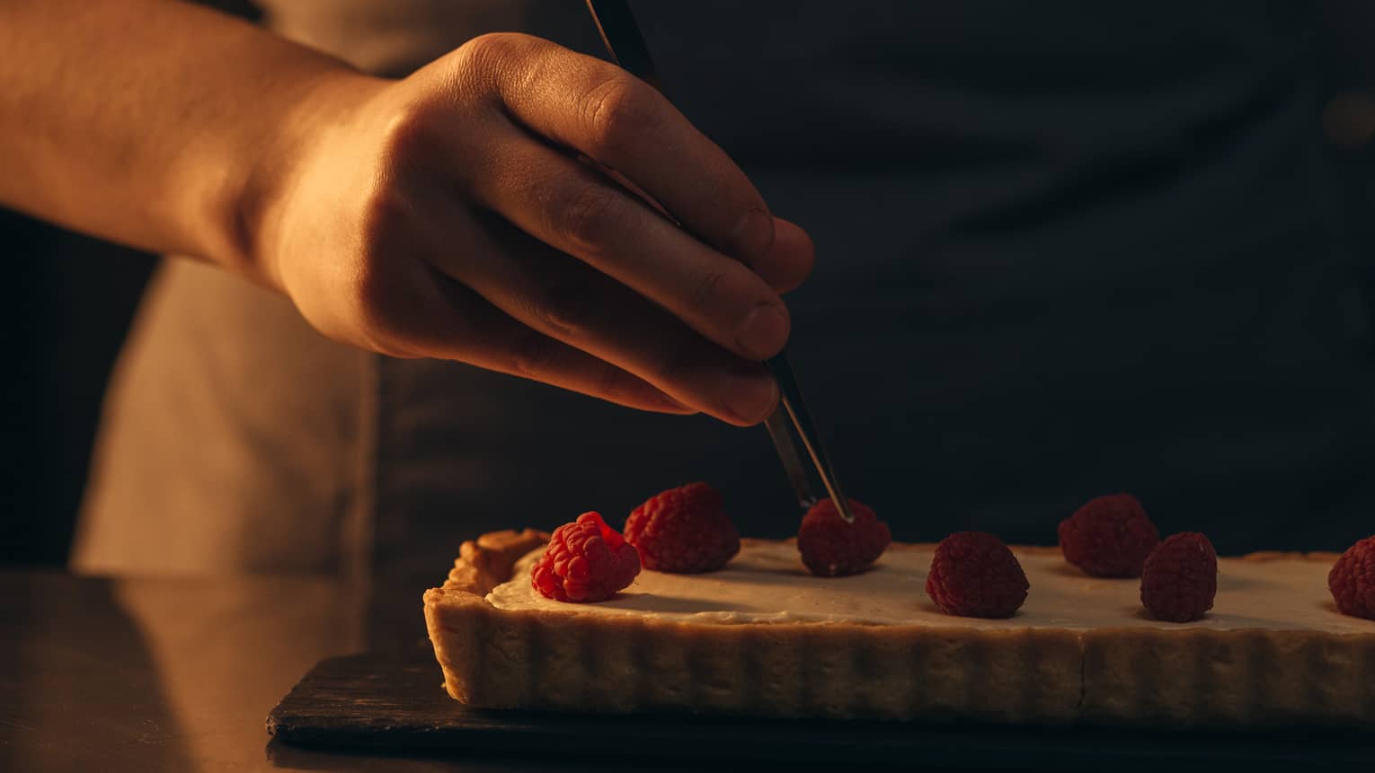 Person putting raspberries onto a dessert.