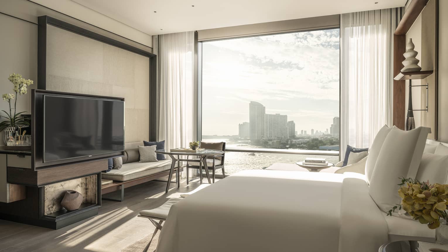Guest room at Four Seasons Hotel Bangkok, with king bed, TV, sitting bench and view of river