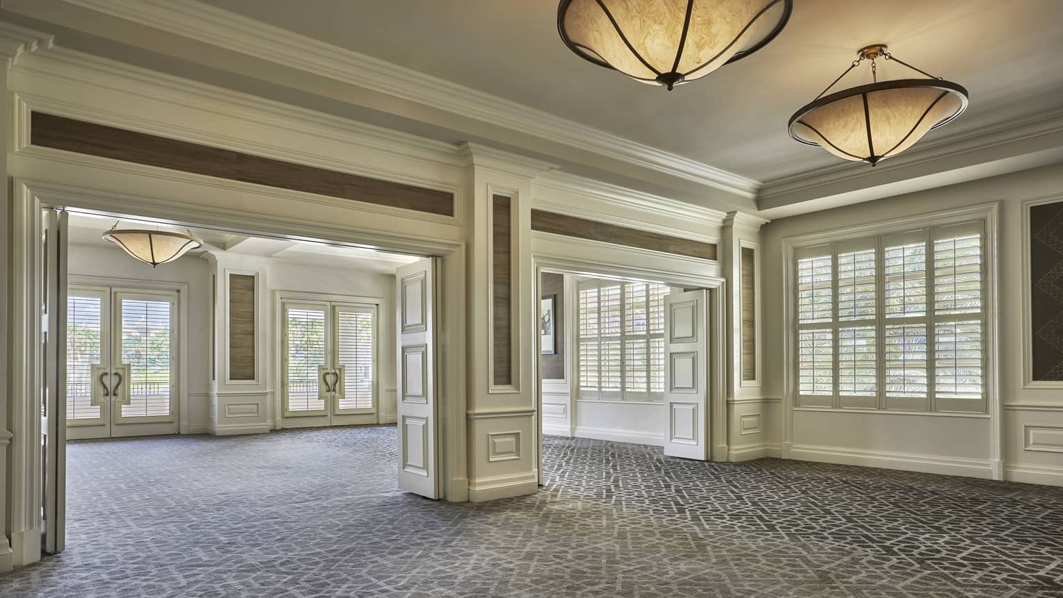 Empty function room with cream-coloured wood panelling and crown molding, grey carpeting