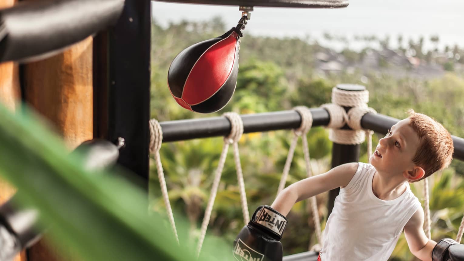 Young boy wearing boxing gloves in ring with small Muay Thai boxing bag