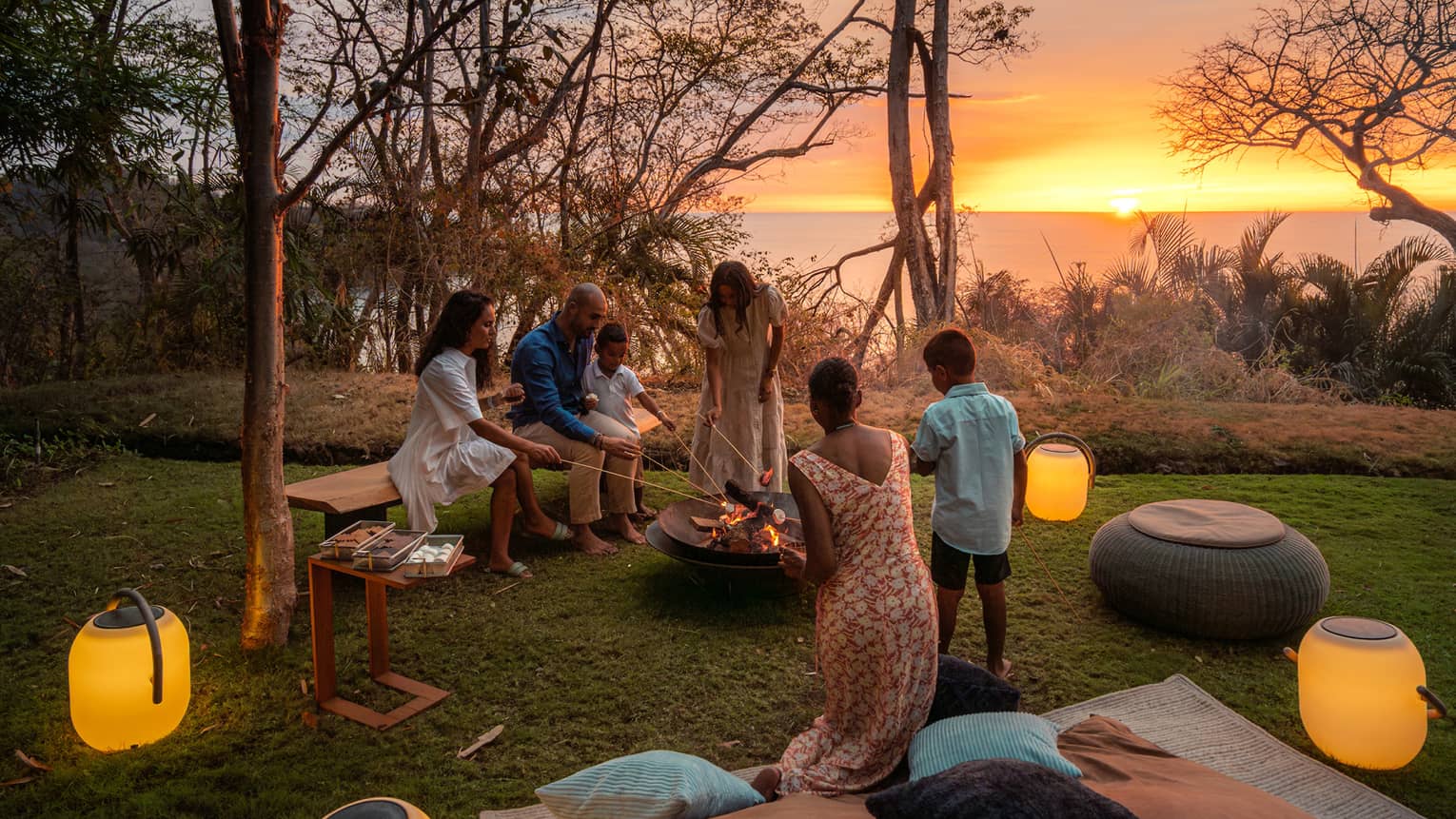Family gathers around a bonfire on a private lawn at sunset