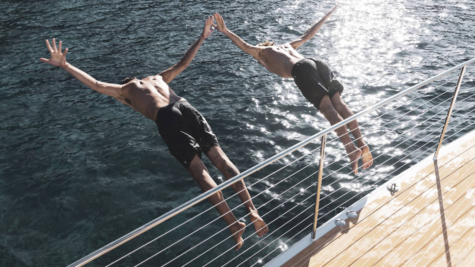Two males dive off a boat into the ocean