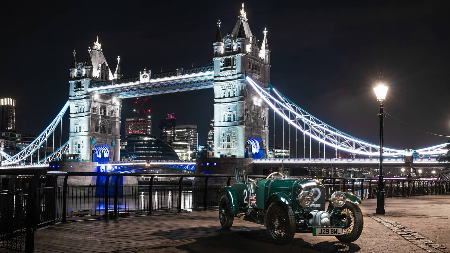 Classic Bentley parked riverside with an uplit Tower Bridge in the backdrop at night