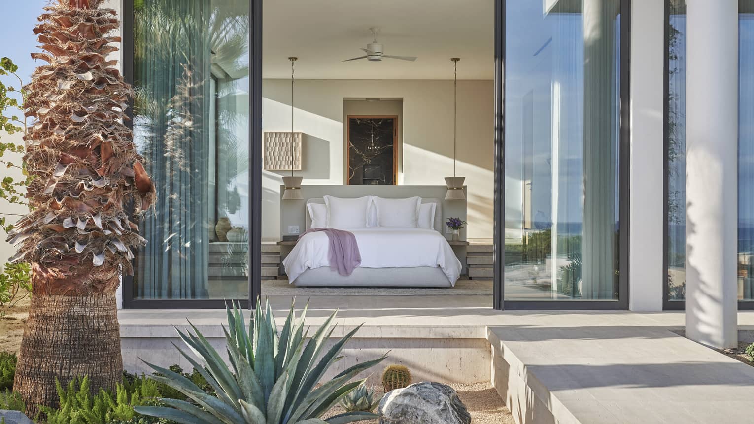 View of a bedroom from outside on a private terrace, through large sliding glass doors, at Four Seasons Resort and Residences Los Cabos