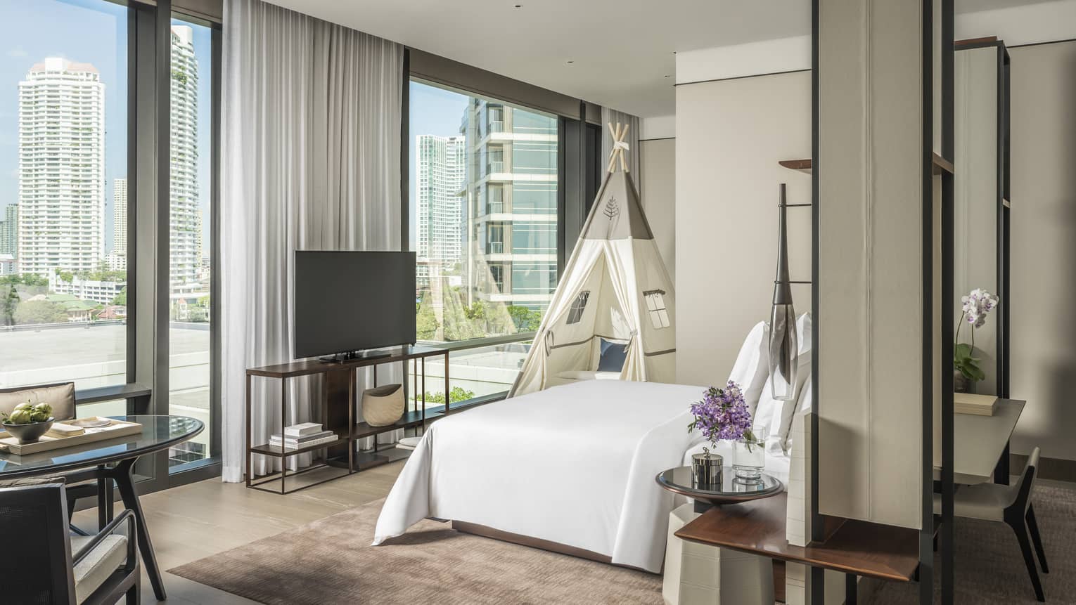 Hotel room with king bed, wall of windows, and kids teepee
