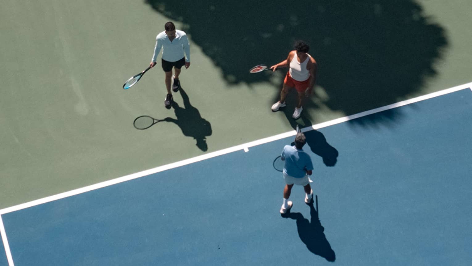 Three people holding tennis racquets on a tennis court.
