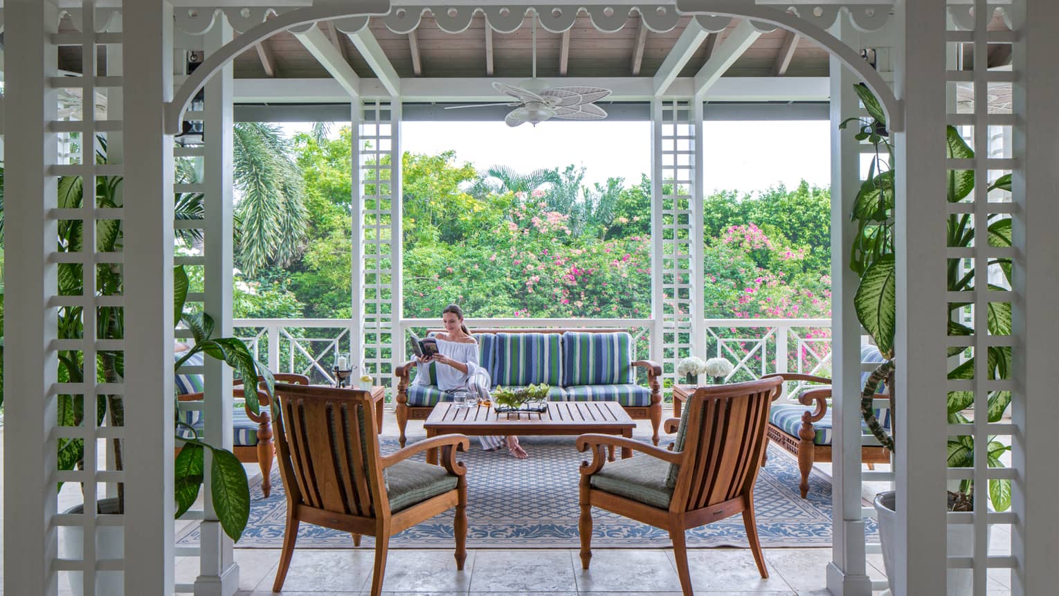 Woman reads book on plush patio sofa by chairs under awning