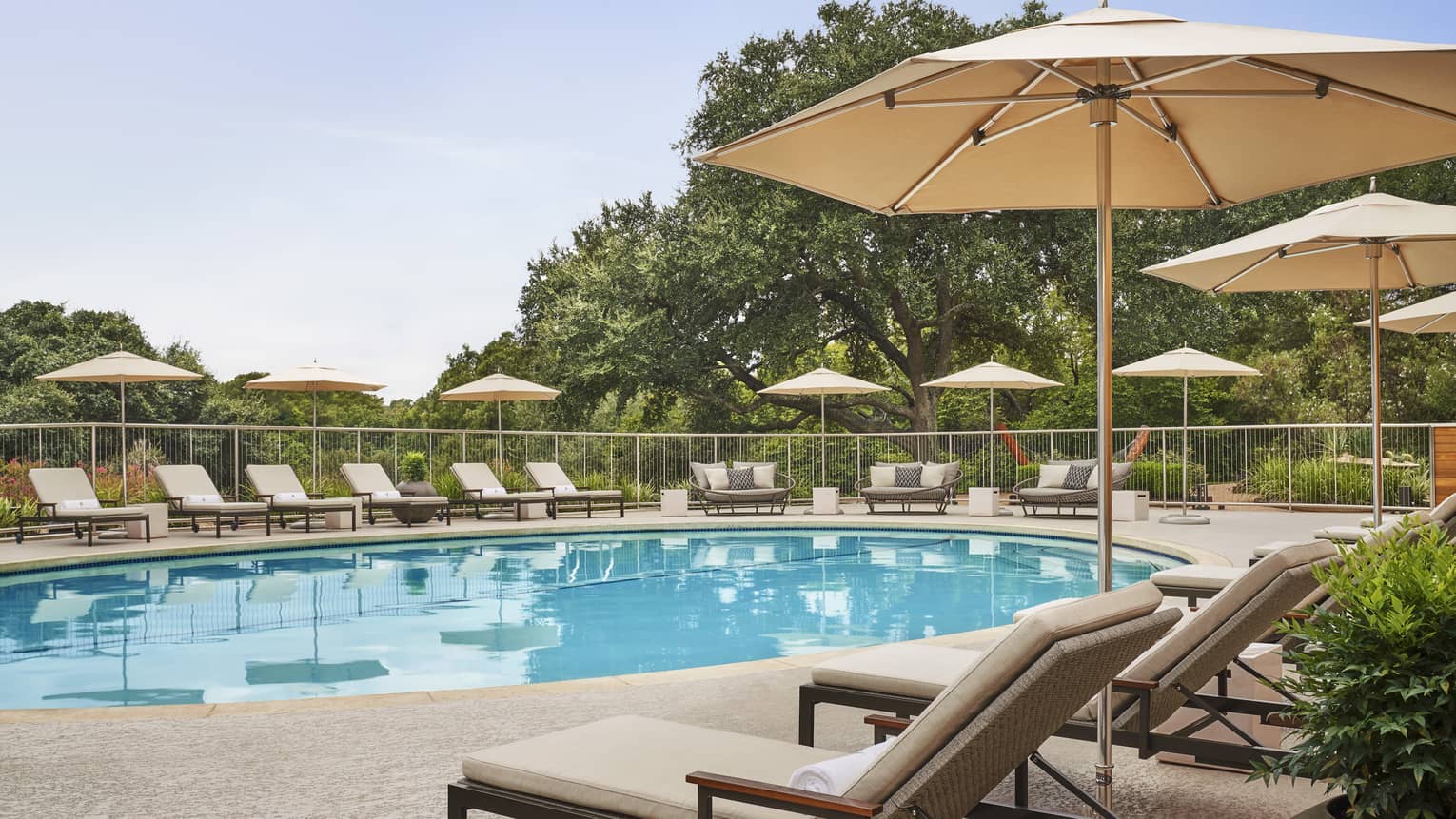 A spacious outdoor pool area with lounge chairs and umbrellas, surrounded by green trees