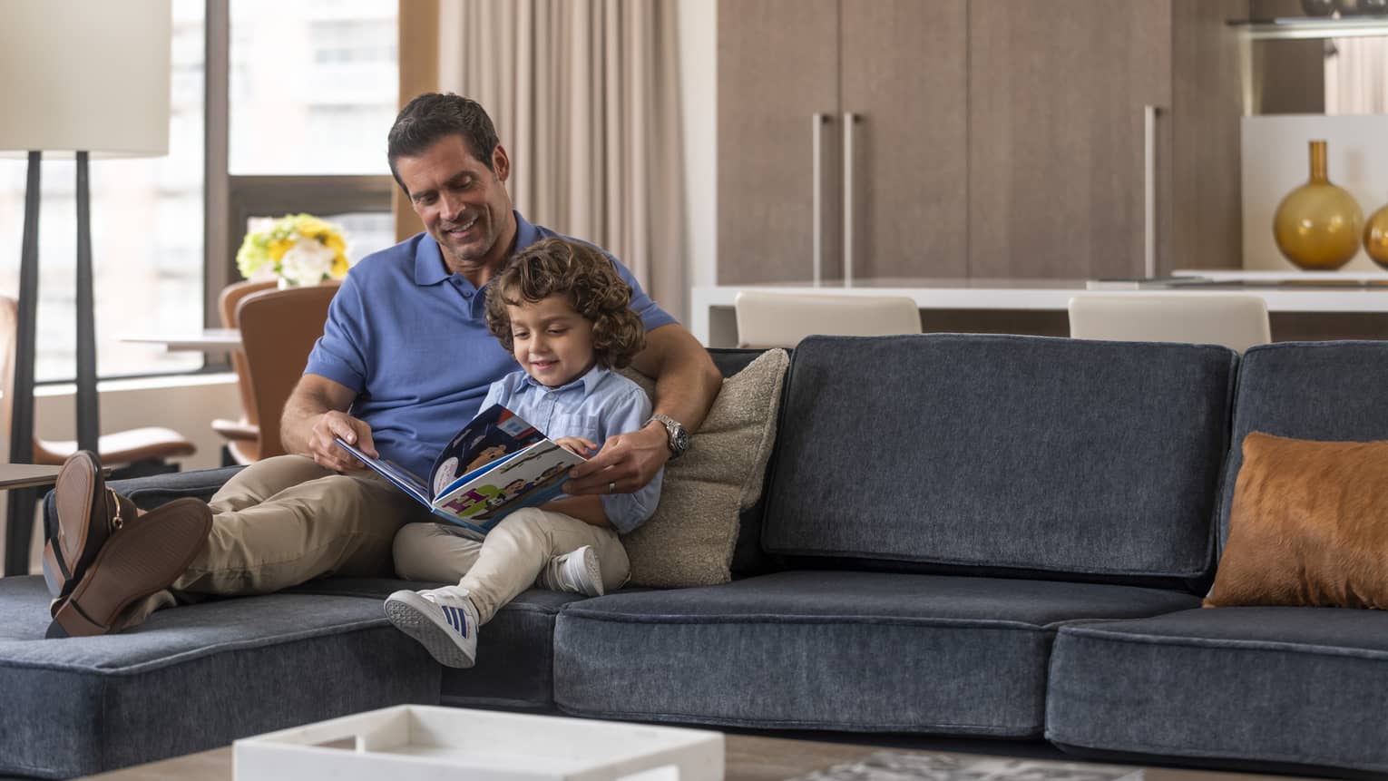 Man sits on a sofa with young boy reading book