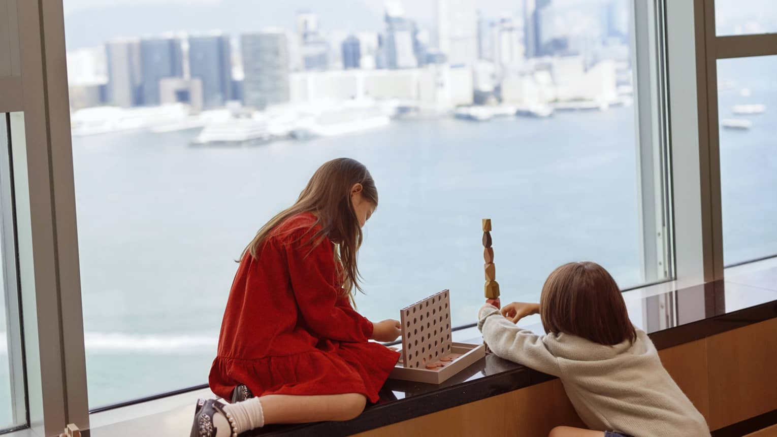 Young children sit on window ledge at hotel, overlooking harbour and city