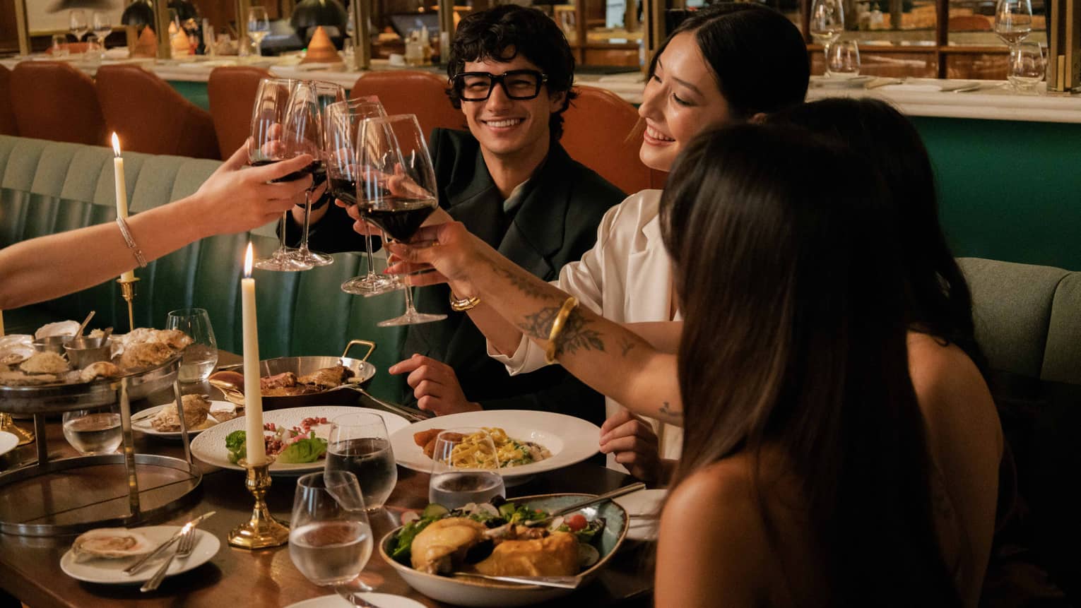 A group clinks glasses of red wine over a dining table filled with various vibrant culinary dishes