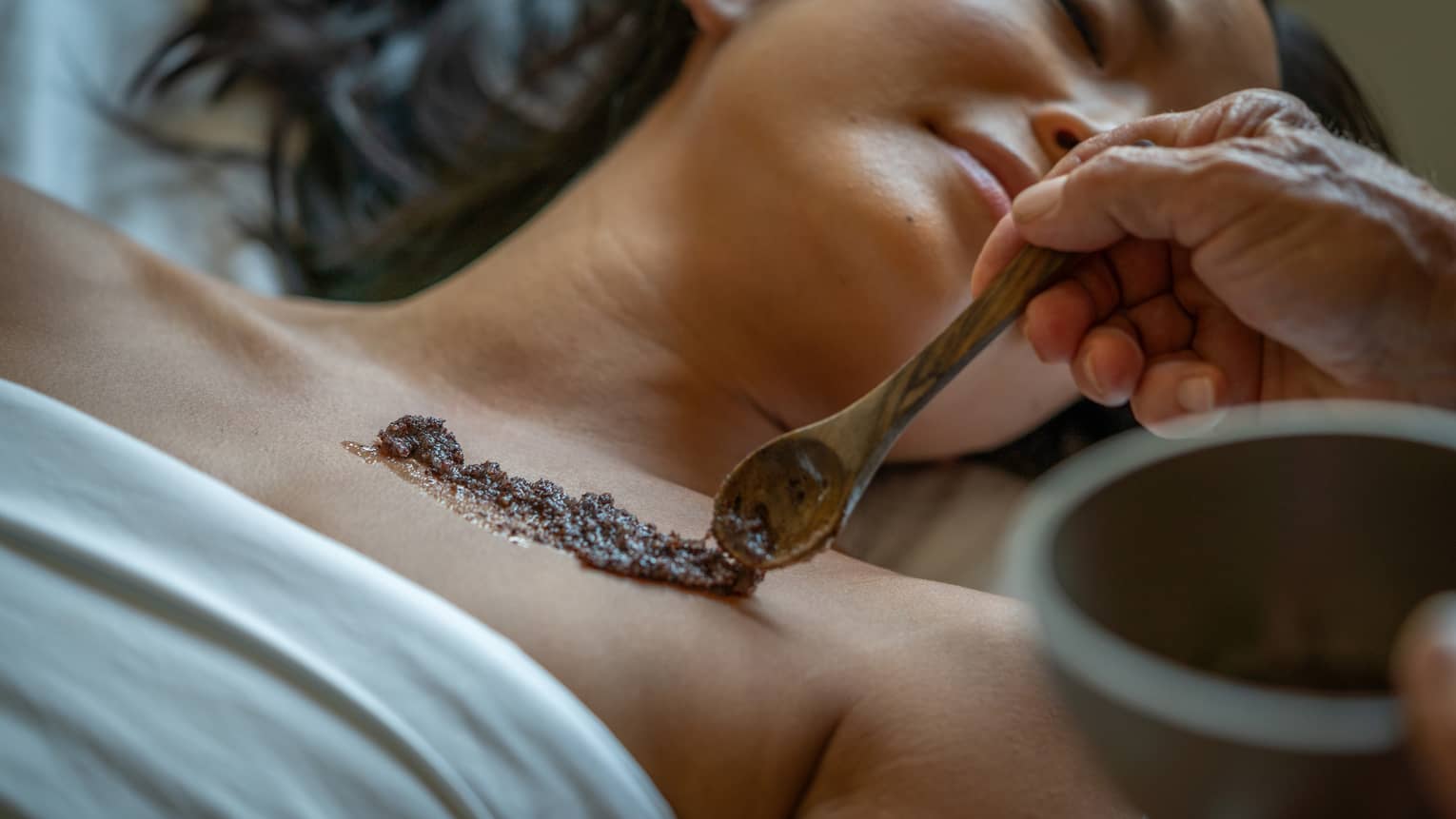 Person laying on a Spa bed while an exfoliating skin scrub is placed on their skin.