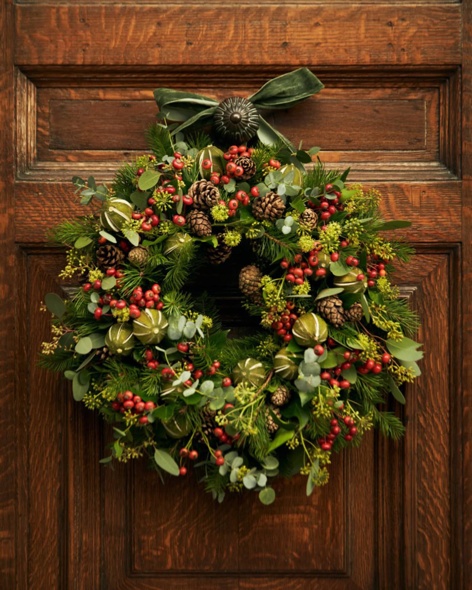 A wreath with red berries hanging on a wood door.