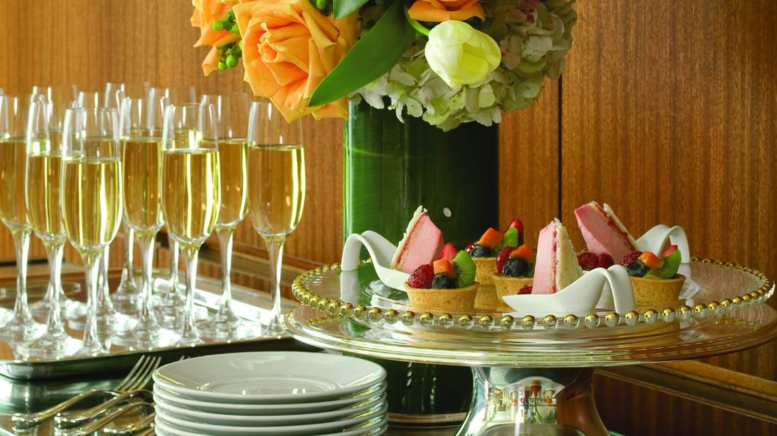 Intricate pastries, cakes and chocolates are arranged on a table next to a flower arrangement and champagne