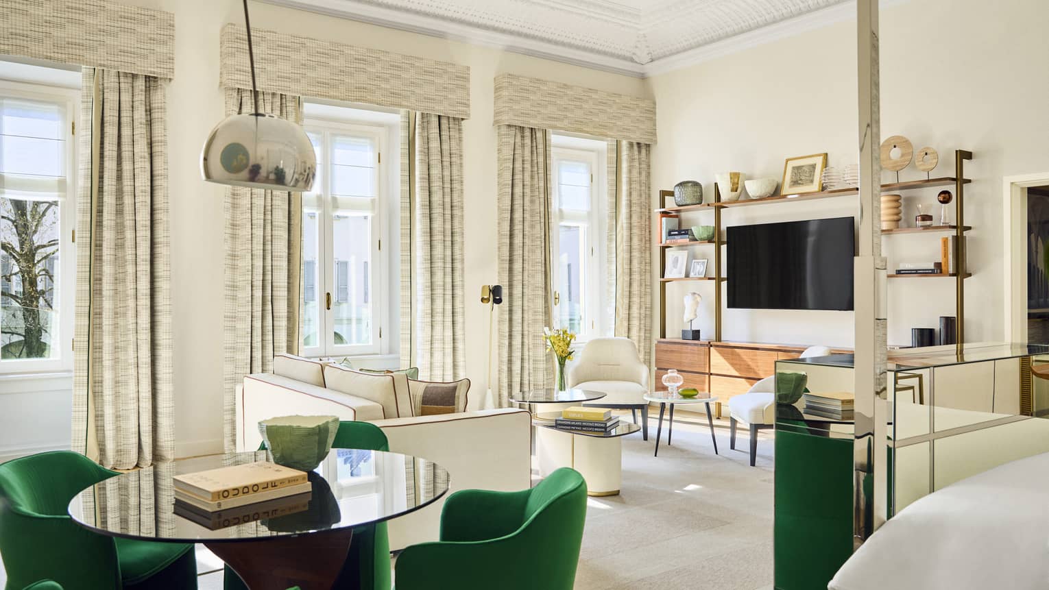 Modern luxury hotel suite with open floor plan, featuring a bed, round dining table with four green chairs, and a living area with a white sofa and two chairs