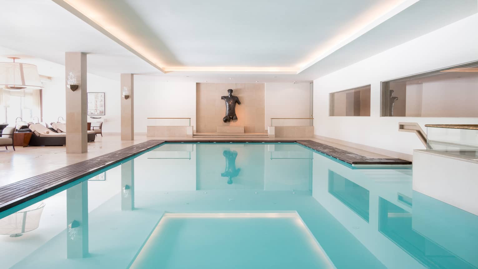 Indoor swimming pool with a modern statue and minimalistic design, featuring clean lines and soft lighting.