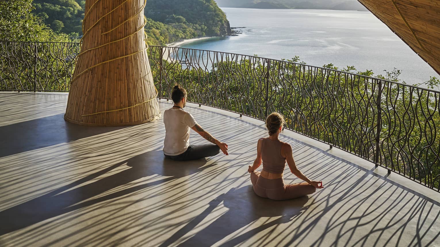 Two people sit cross-legged beneath a wellness pavillion overlooking the ocean below