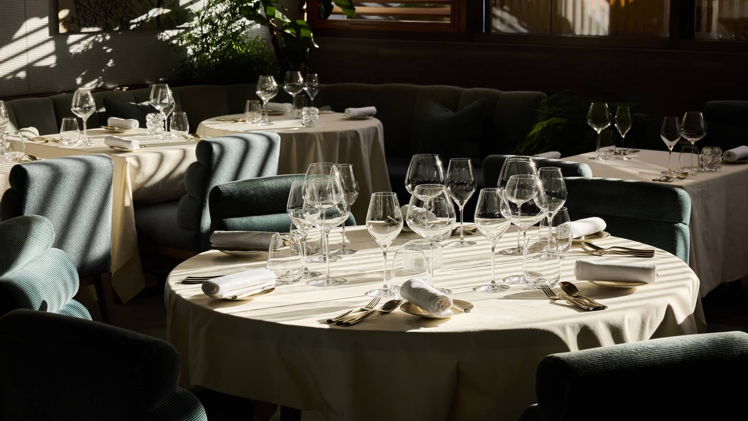 An indoor dining space with dramatic daylight filtering through window blinds and featuring tables, chairs, and place settings for a meal