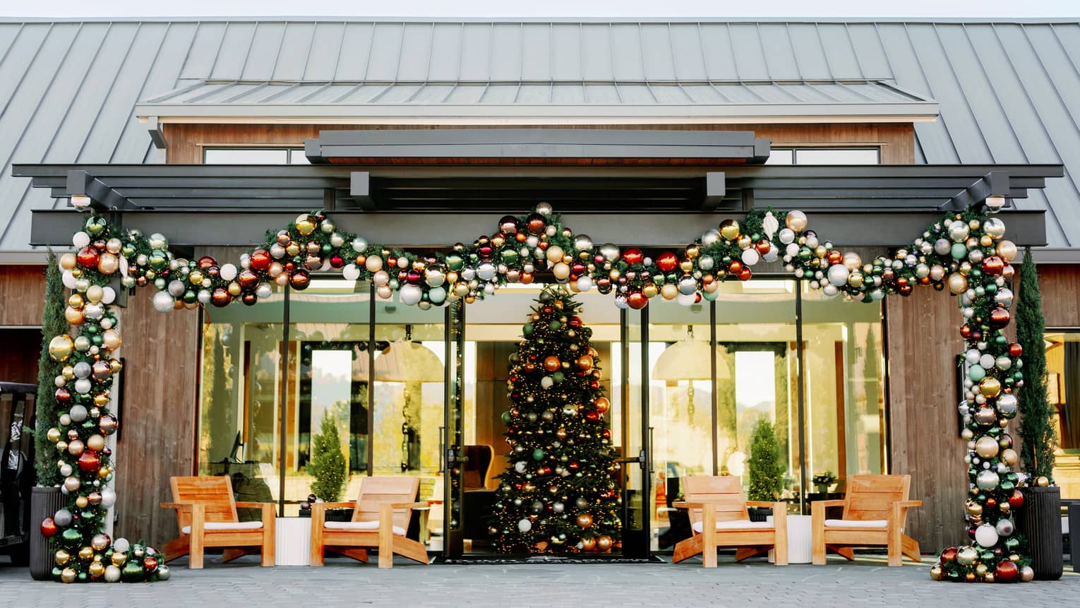 Garland and colourful ornaments frame a glass-fronted entrance to a room with a large, colourfully decorated Christmas tree.