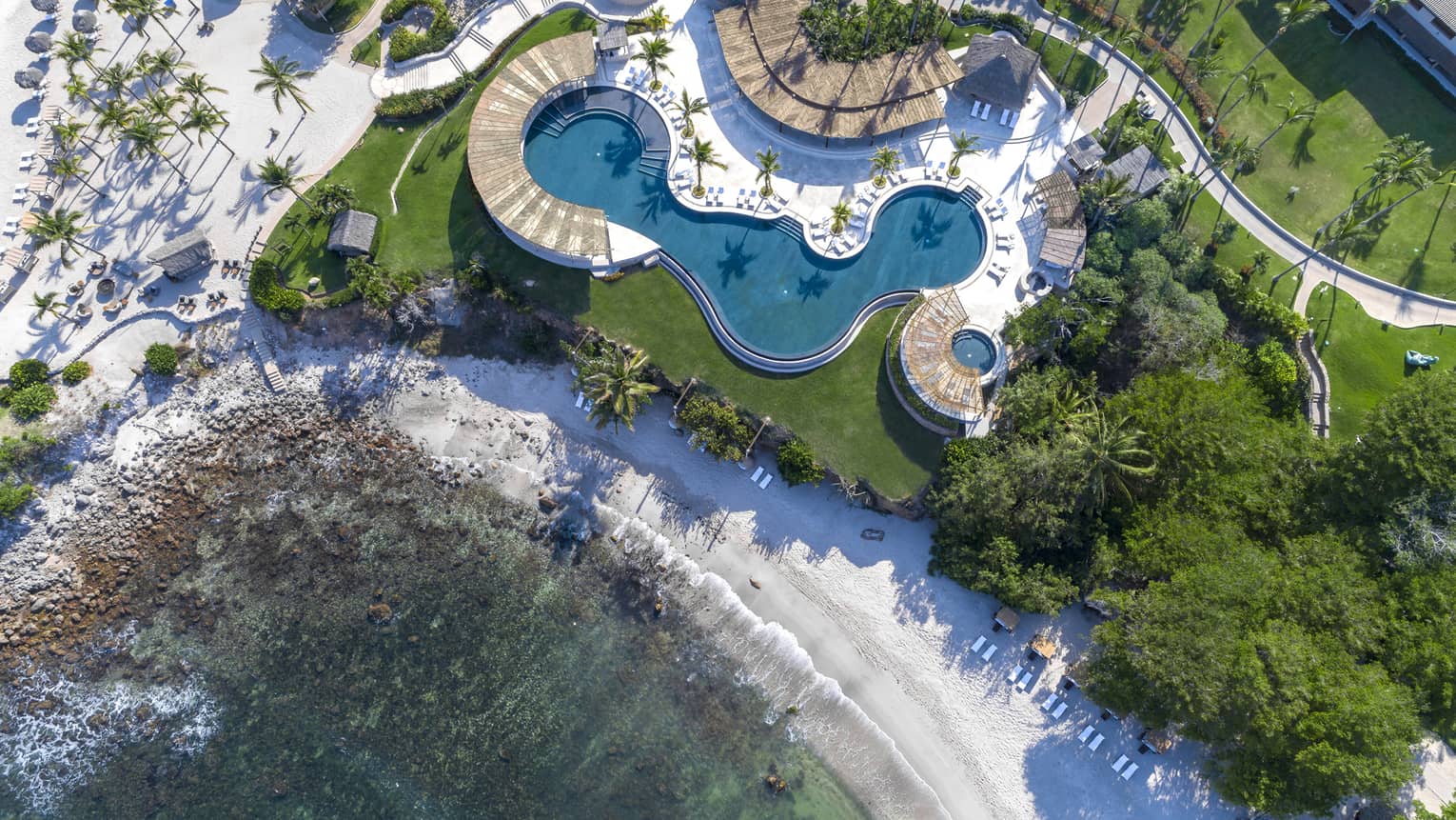 An overhead view of a hotel with a large pool near a beach shore.