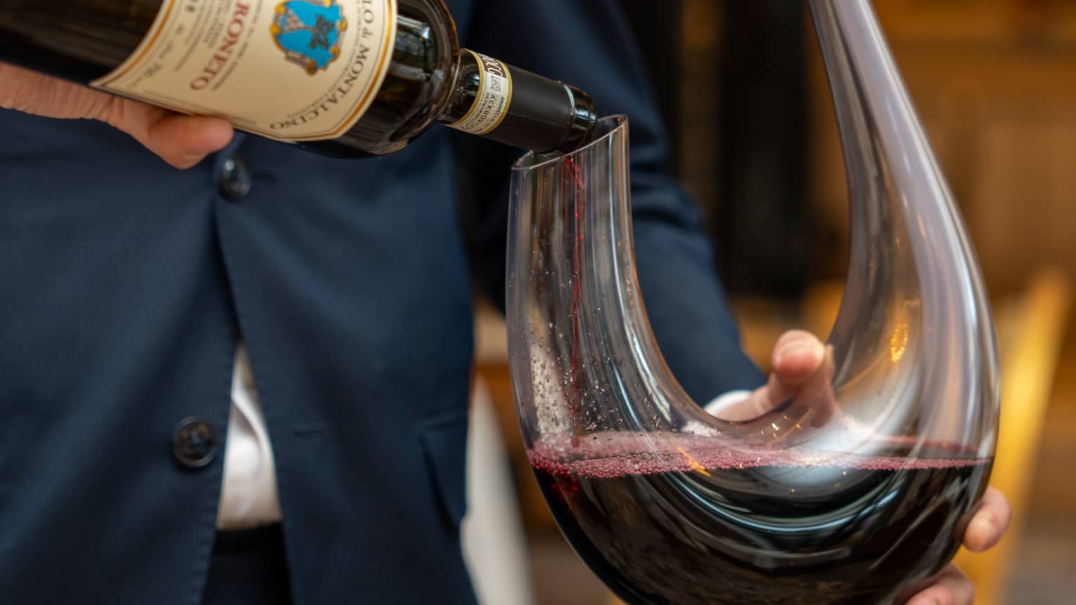 Close-up of a sommelier pouring a bottle of red wine into a U-shaped glass decanter.