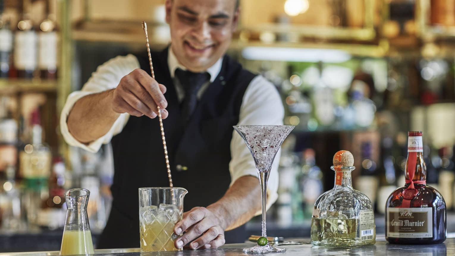 Bartender stirs cocktail with large swizzle stick on bar
