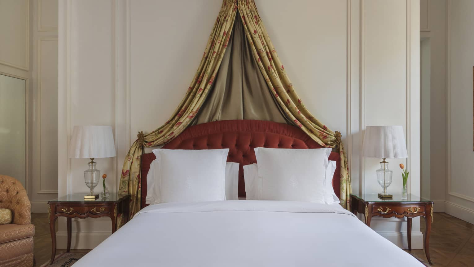 Hotel bed with white linens, red tufted headboard and gold curtains draped overhead