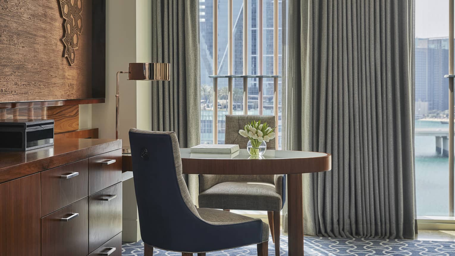 Elegant workspace in a hotel room with a wooden desk, modern chair, tulip centerpiece and floor-to-ceiling windows overlooking a cityscape