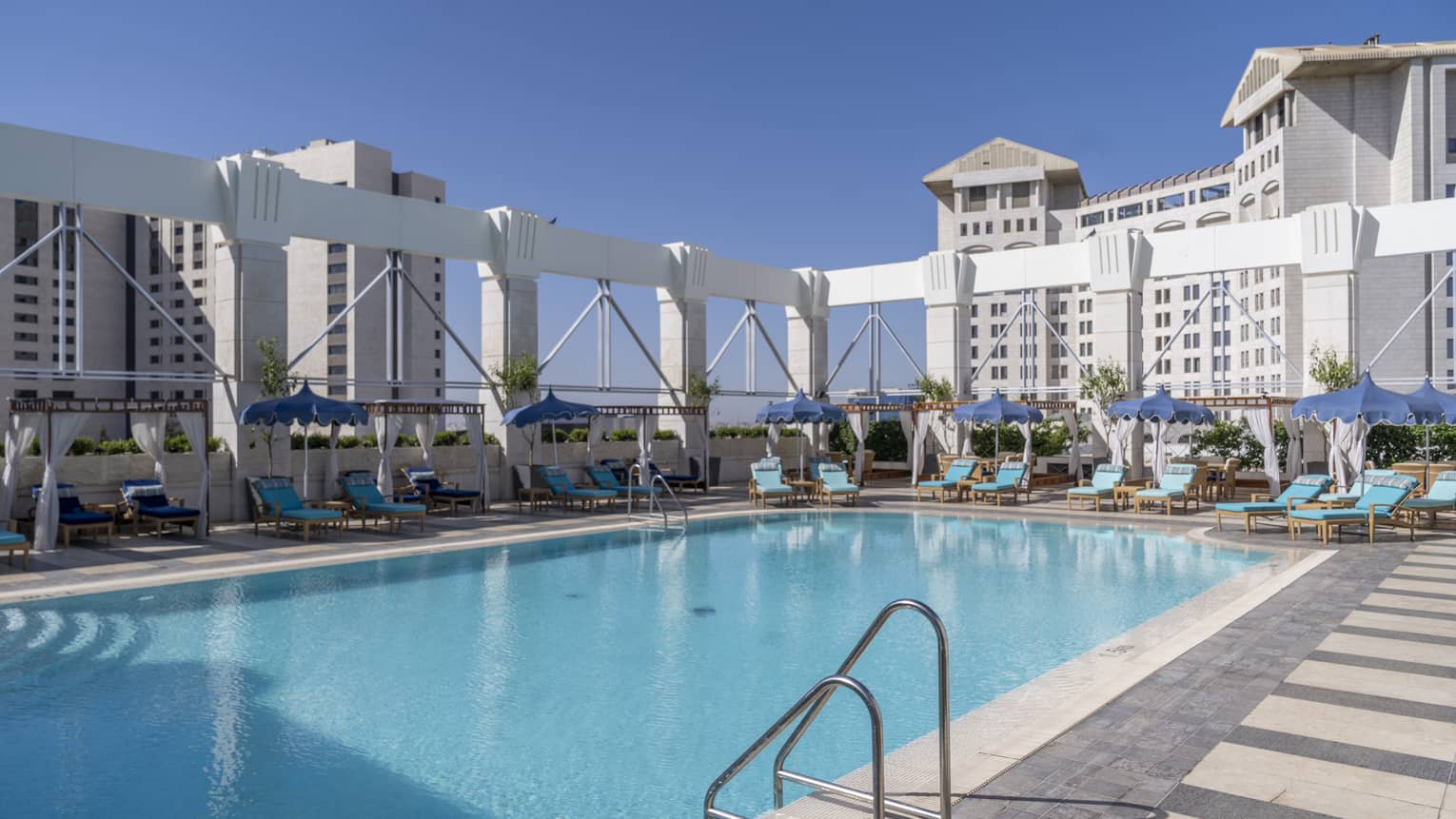 Outdoor pool surrounded by teal lounge chairs and white columns