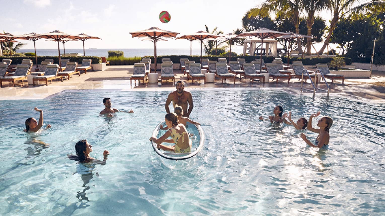 Guests in the pool with palm trees and the ocean in the background.