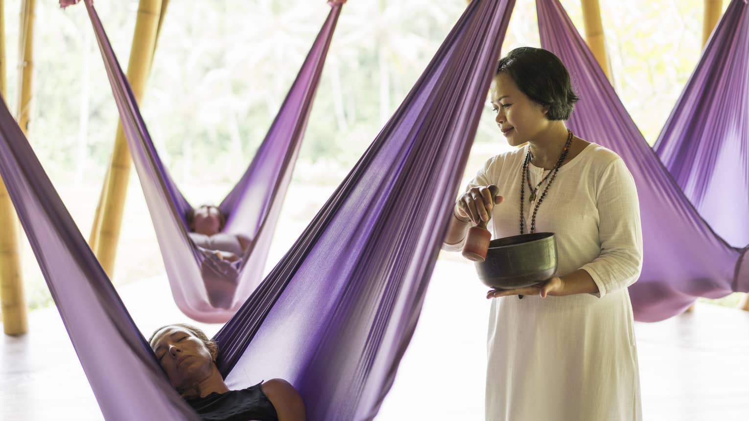 Guests nap in hanging silk hammocks while an instructor plays a sound bowl.