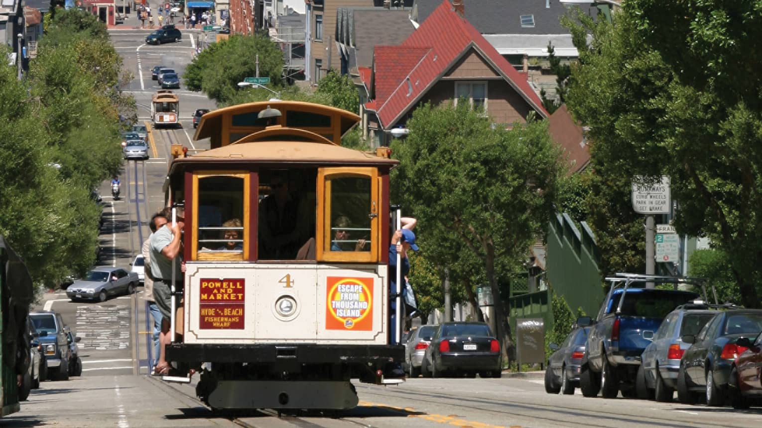 A trolly moving along a city street with water and island, and boats, in the distance.