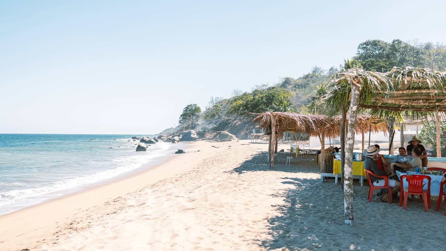The ocean and shore with people sitting together on the sand.