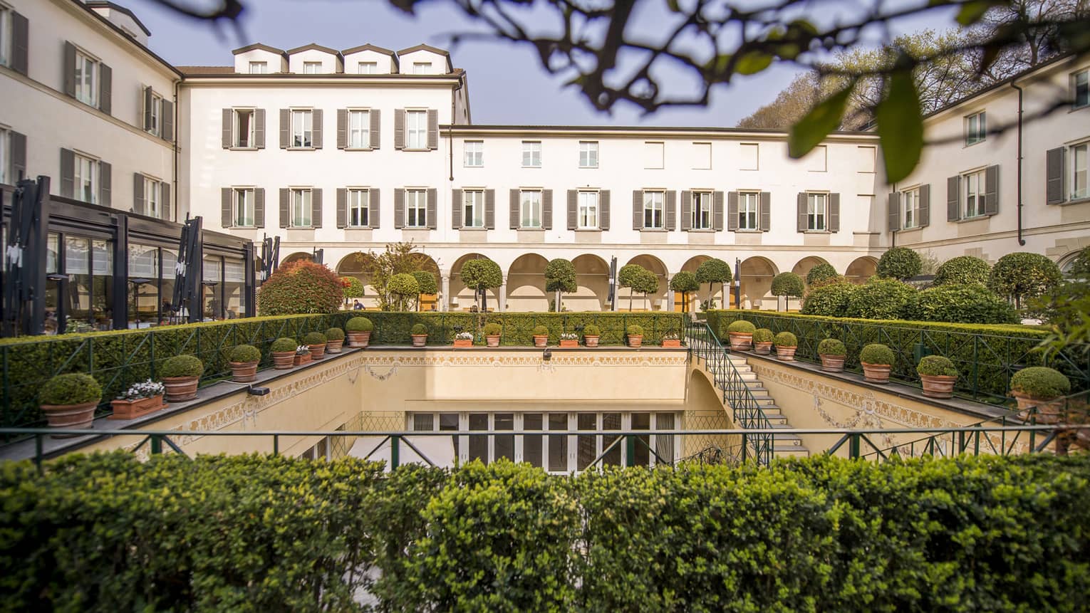 Shrubs, potted plants around rectangular courtyard garden under Four Seasons Hotel Milan building