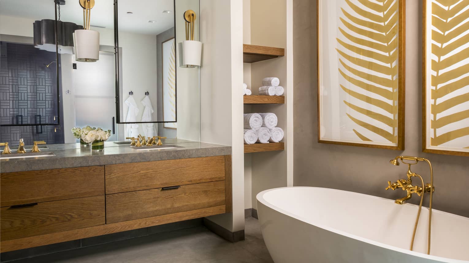 Luxury resort bathroom with wooden double vanity, mirrors, gold fixtures, freestanding tub, built-in towel shelves and botanical wall art
