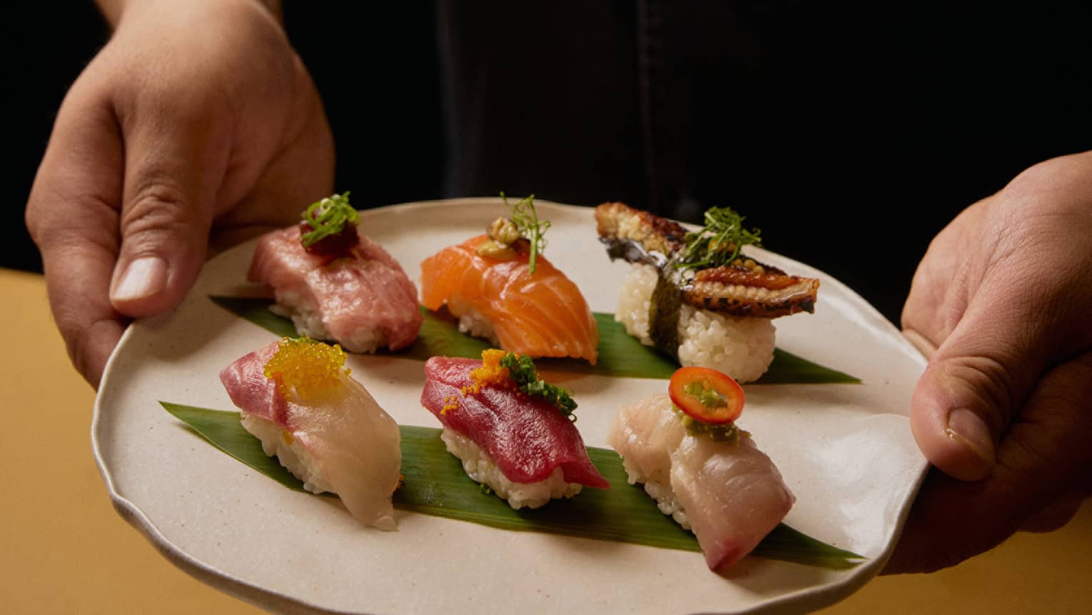 A person in a black shirt holds a plate with six different pieces of sushi.