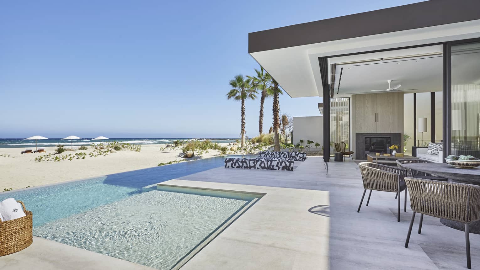 Beside an indoor-outdoor patio, a clear infinity pool overlooks a grassy beach and the breaking waves of the ocean beyond.